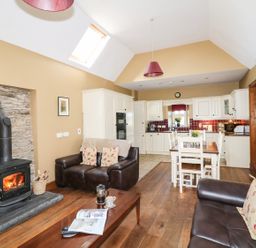 An open living room and kitchen with wood stove and brown leather sofas at Rosemount Coach House Ballycarney near Enniscorthy County Wexford
