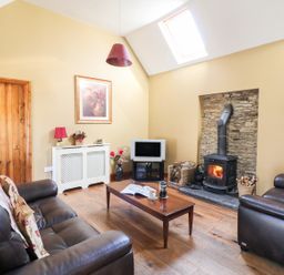 A living room with two leather sofas a wooden coffee table a wood-burning stove and a television at Rosemount Coach House Ballycarney near Enniscorthy County Wexford