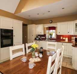 A kitchen with white cabinets wooden dining table and chairs with mugs and scones at Rosemount Coach House Ballycarney near Enniscorthy County Wexford