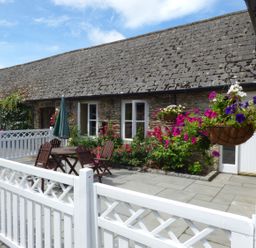 A stone cottage patio with a wooden table and chairs white fencing and hanging flower baskets at Rosemount Coach House in Ballycarney near Enniscorthy County Wexford