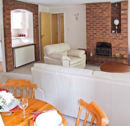 A living room with white sofas a wooden dining table with chairs and a brick fireplace at 9 Bancroft Place in Stratford-upon-Avon