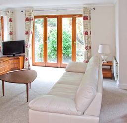 A living room with a white sofa wooden coffee table television and wooden dining chairs at 9 Bancroft Place in Stratford upon Avon