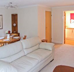 A living room with white sofas a wooden dining table with chairs and a vase with flowers and a kitchen visible through a doorway at 9 Bancroft Place Stratford-upon-Avon