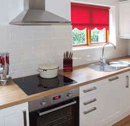A kitchen with a wooden countertop a stovetop with a pot a stainless steel oven a knife block a sink and red window blinds at 9 Bancroft Place in Stratford upon Avon