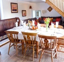 A dining area with a wooden table set with plates and napkins surrounded by wooden chairs and a wooden bench at Woodstone Barn in Whitchurch near Tavistock