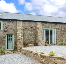 Stone barn exterior with green door windows potted plants bench and gravel courtyard at Woodstone Barn Whitchurch near Tavistock