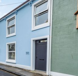 The exterior of a blue two-story building with white trim and a gray door next to a green wall on a street at Barafundle House Tenby