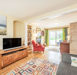 A living room with a wooden TV stand a red armchair and sliding glass doors leading outside at Barafundle House in Tenby