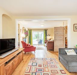 A living room with a gray sofa pillows a patterned rug a wooden cabinet with a television and a red armchair near sliding glass doors at Barafundle House in Tenby