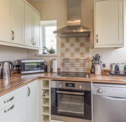 A kitchen with wooden countertops white cabinets a microwave kettle toaster oven and dishwasher at Dune View in Beadnell