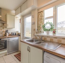 A kitchen with a stainless steel oven dishwasher sink and window with floral curtains at Dune View in Beadnell