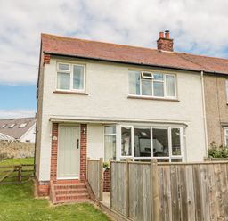 A semi detached house with a white front door and a wooden fence in the front garden at Dune View in Beadnell