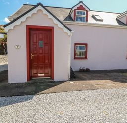 A pink exterior of a cottage with a red door at Fuschia Cottage, Waterville, County Kerry