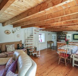 A living room with a sofa, table, and staircase at Fuschia Cottage, Waterville, County Kerry