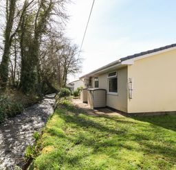 A yellow house next to a small flowing stream and grassy yard at 3 Rosecraddoc Lodge Rosecraddoc Lodge near Liskeard