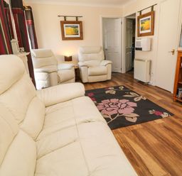 A living room with white leather sofas a floral rug a wooden cabinet with a television and games at 3 Rosecraddoc Lodge Rosecraddoc Lodge near Liskeard