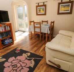 A living room with a cream sofa wooden dining table with chairs and a television on a wooden stand at 3 Rosecraddoc Lodge in Rosecraddoc Lodge near Liskeard