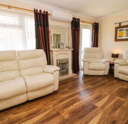 A living room with cream leather sofas a fireplace a mirror curtains a side table with a lamp and a framed picture on the wall at 3 Rosecraddoc Lodge Rosecraddoc Lodge near Liskeard