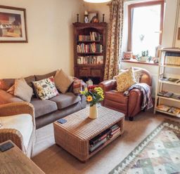 A living room with a sofa, armchairs, a coffee table with flowers, bookshelves, and a window at Lothlorien Cottage in Cwmgors near Ammanford