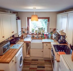 A kitchen with wooden countertops a washing machine a microwave a stove and a sink with plants on the windowsill at Lothlorien Cottage in Cwmgors near Ammanford