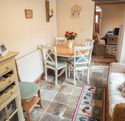 A dining area with a round table and four chairs a cabinet a chair and a sofa at Lothlorien Cottage in Cwmgors near Ammanford