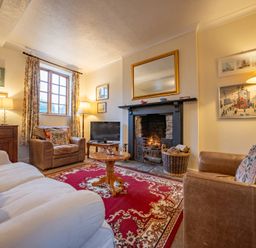 A living room with two armchairs a sofa a fireplace with a fire a red patterned rug and a wooden table at The Coach House in Gilwern near Crickhowell and Abergavenny