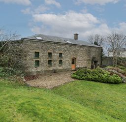 A stone building with small windows a wooden door a garden with bushes and grass at The Coach House in Gilwern near Crickhowell and Abergavenny
