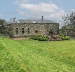 An exterior view of a stone building with small windows and a door in a grassy garden at The Coach House in Gilwern near Crickhowell and Abergavenny