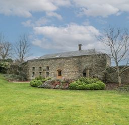 A stone building with small windows and a wooden door surrounded by grass and bushes at The Coach House in Gilwern near Crickhowell and Abergavenny