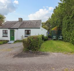 A white cottage with a green door and windows a gravel driveway and a garden with hedges and two plastic chairs at Brendans Cottage in Valentia Island County Kerry