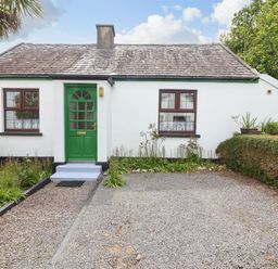 A white cottage with green door and windows surrounded by gravel driveway and trimmed bushes at Brendans Cottage in Valentia Island County Kerry