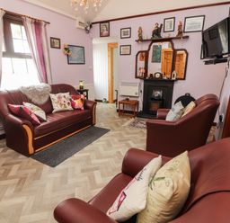 A living room with maroon leather sofas, floral cushions, a fireplace, a wall-mounted TV, and decorative items at Brendan's Cottage in Valentia Island County Kerry