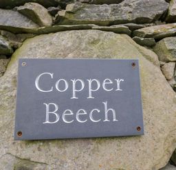 A sign reading Copper Beech mounted on a stone wall at Copper Beech Cottage in Torver