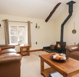 A living room with a wood burning stove and seating at Copper Beech Cottage in Torver