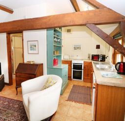 A small kitchen and sitting area with wooden beams a white armchair a television and kitchen appliances at The Pottery in Urchfont near Devizes