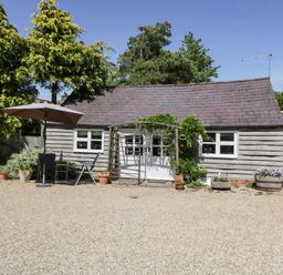 A small wooden building with a tiled roof surrounded by trees and plants at The Pottery in Urchfont near Devizes