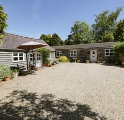 A courtyard with gravel ground surrounded by wooden buildings and various potted plants at The Pottery in Urchfont near Devizes
