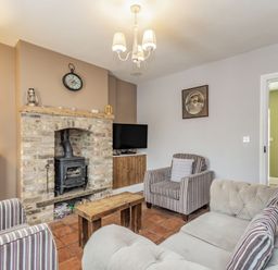 A living room with a brick fireplace and wood stove two striped armchairs a beige sofa a wooden coffee table a TV and a bookshelf at Fisher Cottage in Hornsea