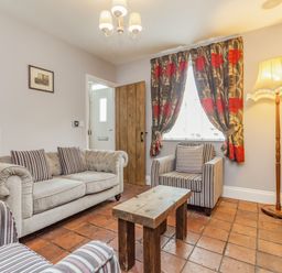 A living room with a beige sofa striped armchairs wooden coffee table floral curtains and a floor lamp at Fisher Cottage in Hornsea