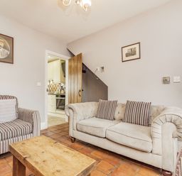 A living room with a striped armchair a wooden table and a beige sofa with striped cushions at Fisher Cottage in Hornsea