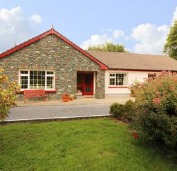 A stone and white house with red trim surrounded by green grass and bushes at The Lodge in Churchtown near Beaufort County Kerry
