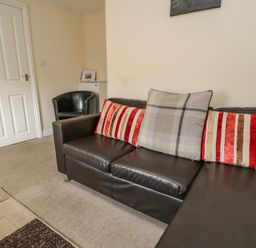 A living room with a black leather sofa with pillows and a black armchair near a closed white door at Cairns Cottage in Whitby