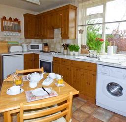 A kitchen with wooden cabinets a dining table set with cups plates and orange juice at The White Cottage in Bridlington