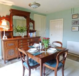 A dining room with a wooden table set for four and a wooden sideboard with a mirror at The White Cottage in Bridlington