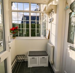 A small enclosed porch with a white storage bench a window shelf with a flower pot and decorations at Ty'r Ysgol in Morfa Bychan