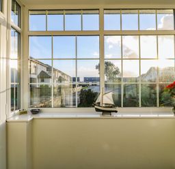A porch area with large windows a model sailboat and a potted plant at Ty'r Ysgol in Morfa Bychan