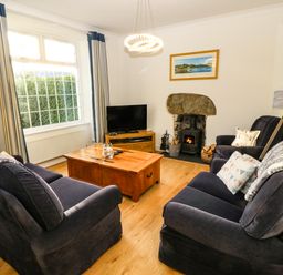 A living room with two dark sofas a wooden coffee table a television a fireplace and large window at Ty'r Ysgol in Morfa Bychan