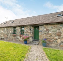 A stone exterior building with green door and windows with flower pots on a gravel path at Foxglove in Newport Pembrokeshire
