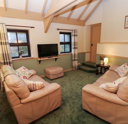 A living room with two beige sofas a wall-mounted TV and green carpet at Foxglove in Newport Pembrokeshire