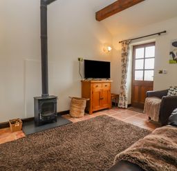 A living room with a wood stove and television on a wooden cabinet at Dairy Barn in Pershore